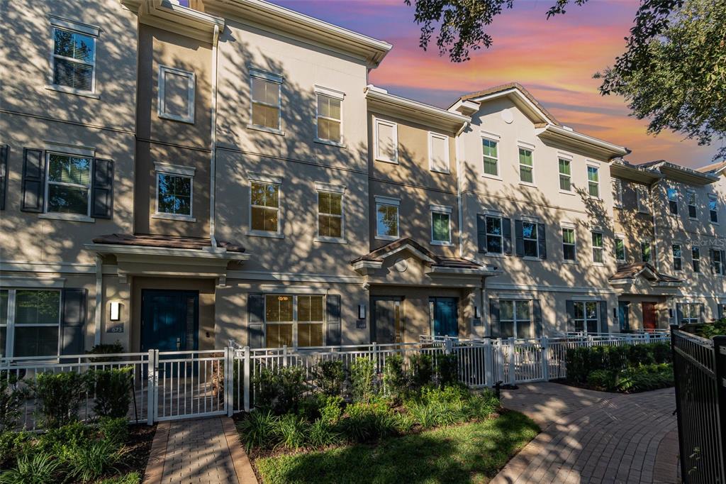 A row of multi-story townhomes with beige stucco facades and white fenced front patios — 669 HANGNEST LANE, LAKE MARY, FL
