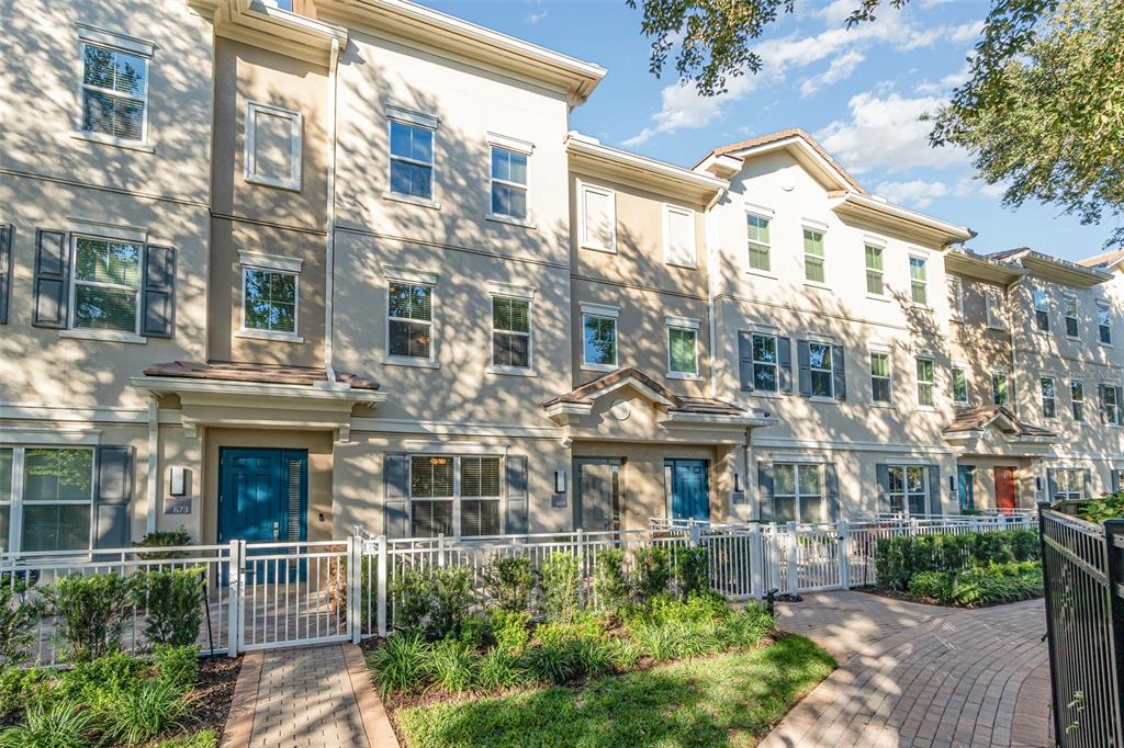 A row of multi-story townhomes with beige stucco facades, blue front doors, and white fencing — 669 HANGNEST LANE, LAKE MARY, FL