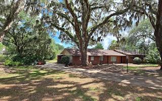A single-story brick house sits on a wooded lot with large, moss-draped oak trees — 5309 COUNTY ROAD 114D, WILDWOOD, FL