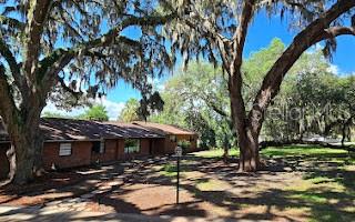 A single-story brick house sits under large oak trees with Spanish moss in a yard — 5309 COUNTY ROAD 114D, WILDWOOD, FL