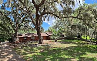 A single-story brick house sits on a grassy lot shaded by large, moss-covered oak trees — 5309 COUNTY ROAD 114D, WILDWOOD, FL
