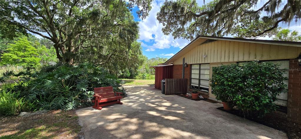 A red wooden bench sits on a concrete patio next to a brick house exterior — 5309 COUNTY ROAD 114D, WILDWOOD, FL
