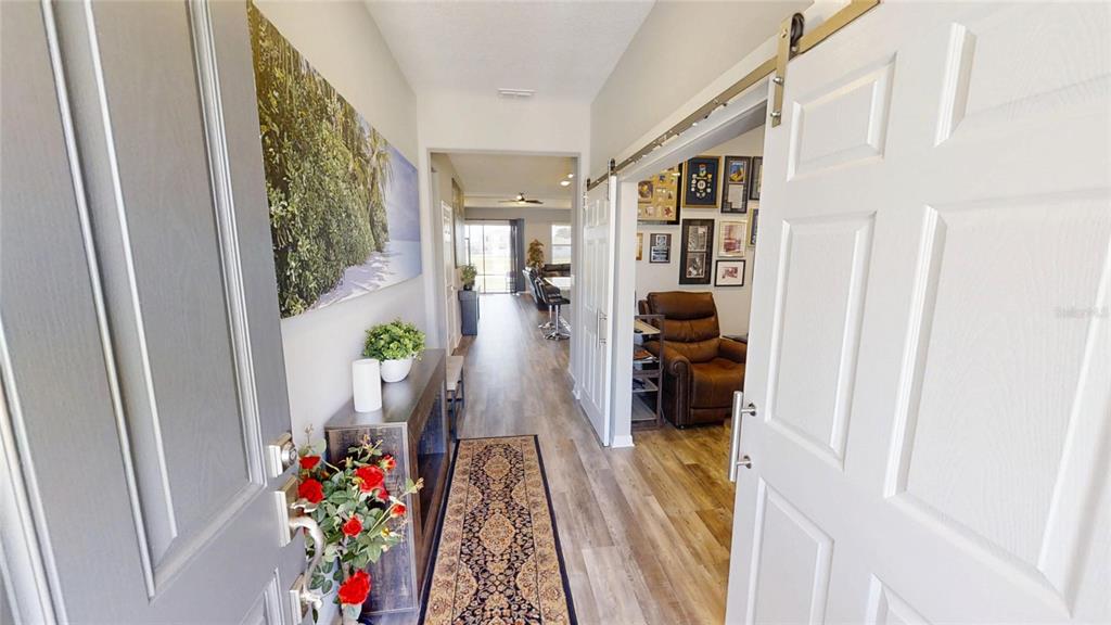 A view from an entryway into a hallway with wood-look flooring and a sliding door — 5655 SW 78TH AVENUE ROAD, OCALA, FL