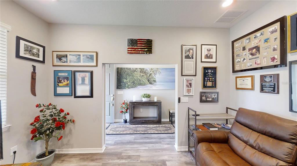 A living room with a brown leather sofa, wall-mounted memorabilia, and a central doorway — 5655 SW 78TH AVENUE ROAD, OCALA, FL