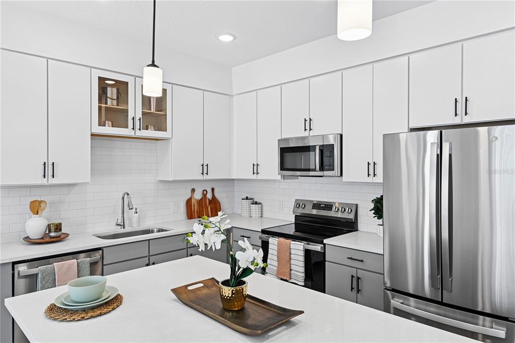 A kitchen features white upper cabinets, gray lower cabinets, stainless steel appliances, and a quartz island — 1898 ZAC STREET UNIT Dawn, KISSIMMEE, FL