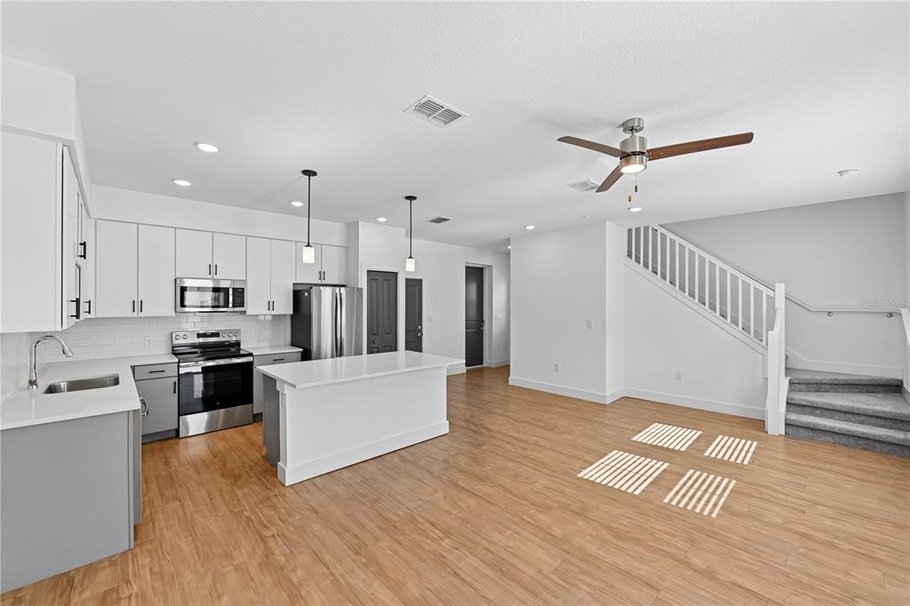 A modern kitchen with white cabinets, stainless steel appliances, and an island opens to stairs — 1898 ZAC STREET UNIT Dawn, KISSIMMEE, FL