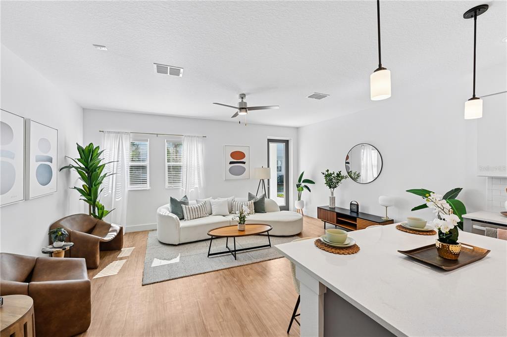 A bright, open-concept living room features a white curved sofa, leather chairs, and wood flooring — 1898 ZAC STREET UNIT Dawn, KISSIMMEE, FL