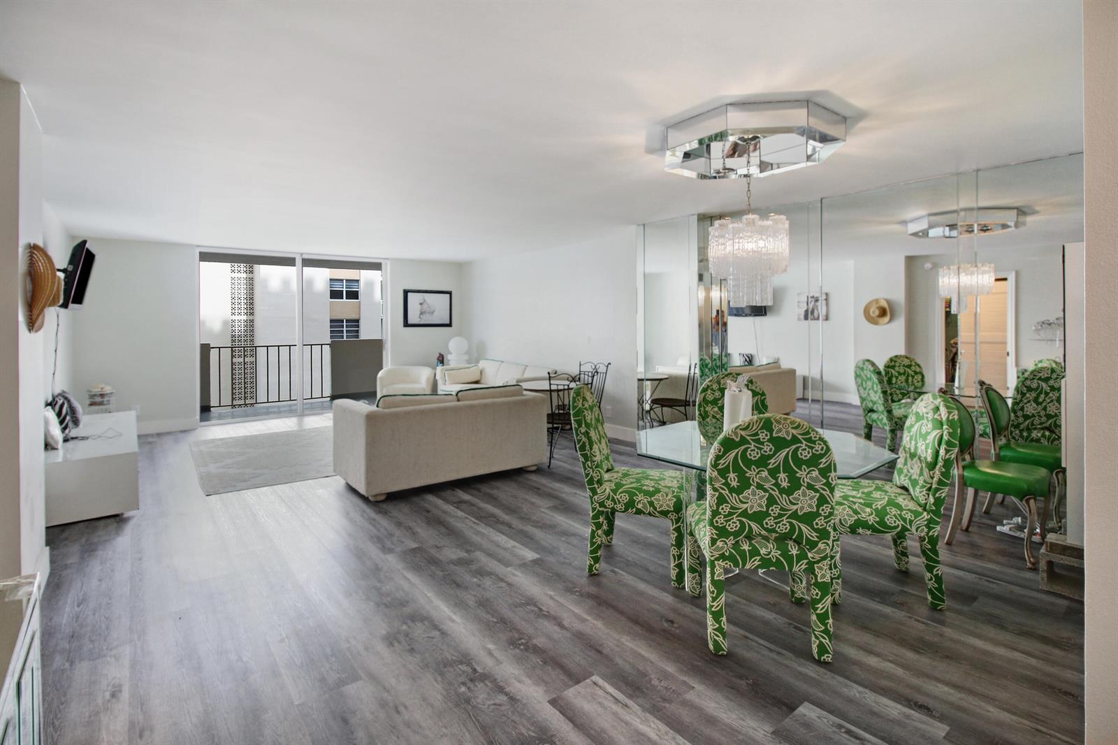 A living and dining area with gray wood-look flooring, green patterned chairs, and mirrored walls — 1865 S Ocean Drive # 6c, Hallandale Beach FL 33009, HALLANDALE BEACH, FL