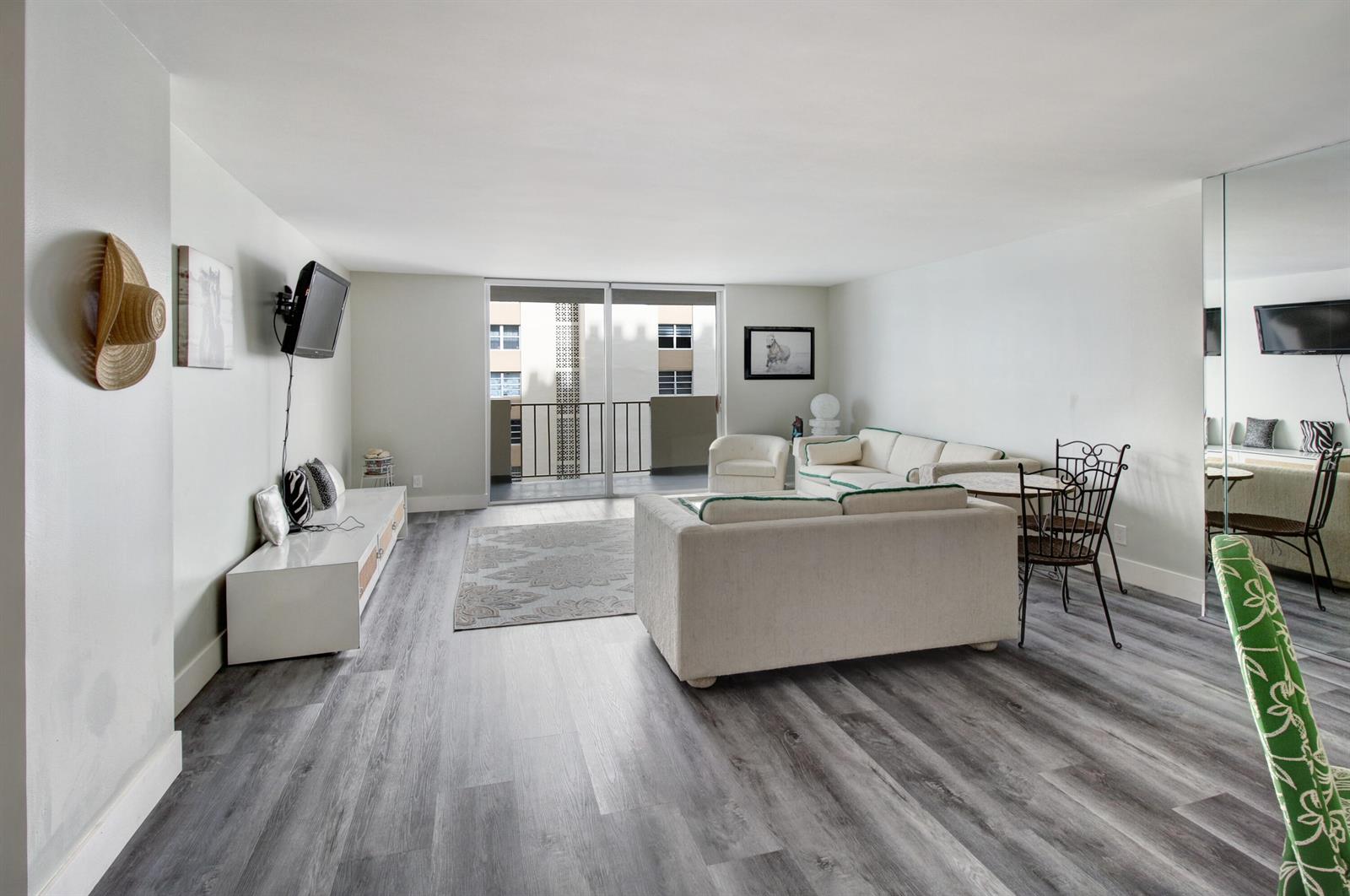 A living room with gray wood-look flooring, white furniture, and a sliding glass balcony door — 1865 S Ocean Drive # 6c, Hallandale Beach FL 33009, HALLANDALE BEACH, FL