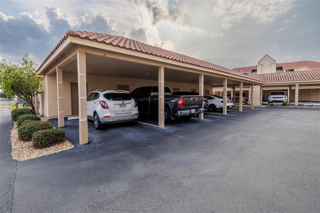 A covered parking area with multiple vehicles parked under a tiled roof structure — 434 BOUCHELLE DRIVE UNIT 203, NEW SMYRNA BEACH, FL