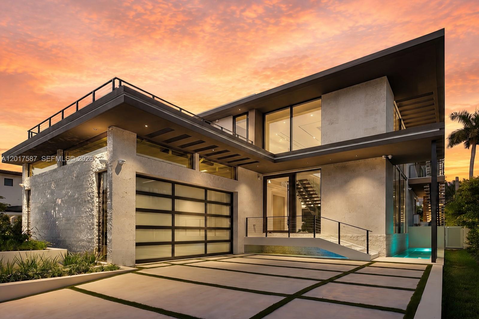 A modern two-story house with a glass garage door, stone facade, and a sunset sky — 3045 N Bay Rd, Miami Beach FL 33140, MIAMI BEACH, FL