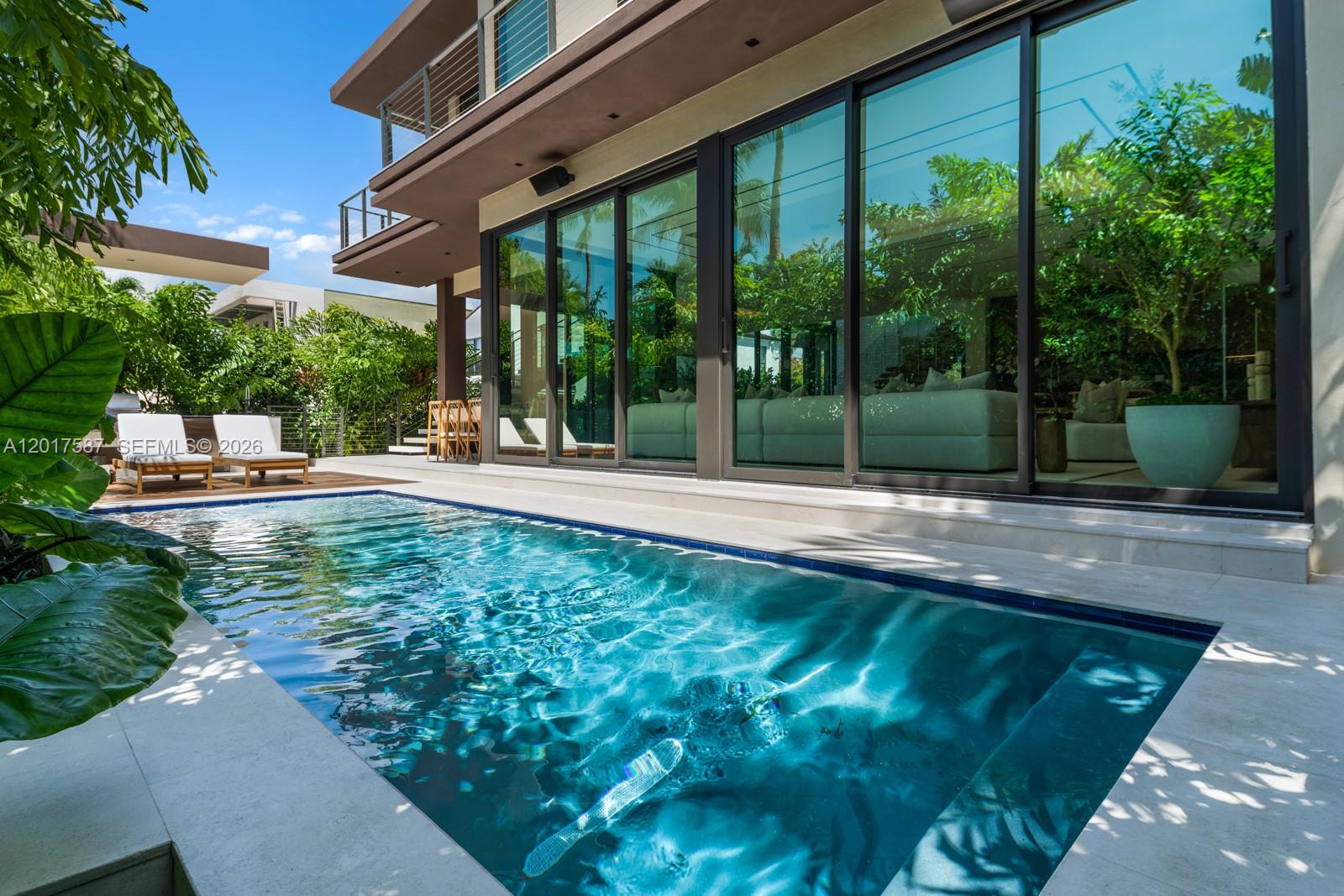 A modern house features a swimming pool, large glass sliding doors, and a wooden deck — 3045 N Bay Rd, Miami Beach FL 33140, MIAMI BEACH, FL