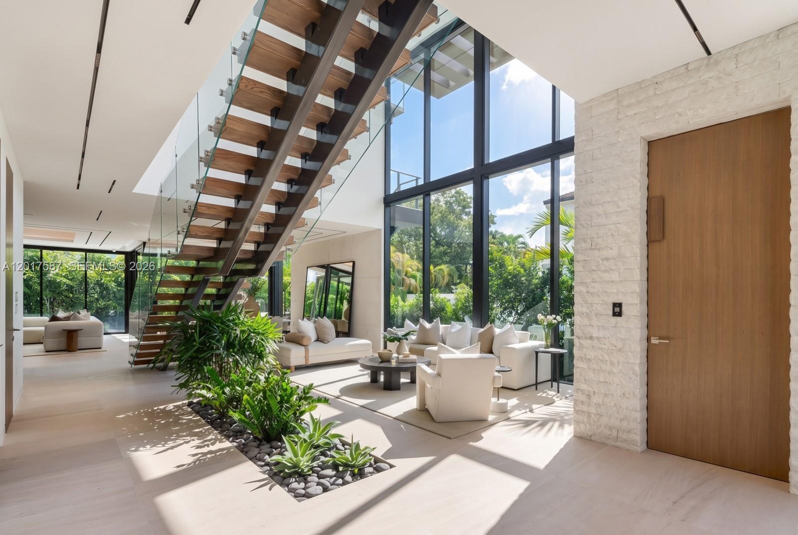 A modern living room features a floating staircase, floor-to-ceiling windows, and an indoor garden bed — 3045 N Bay Rd, Miami Beach FL 33140, MIAMI BEACH, FL