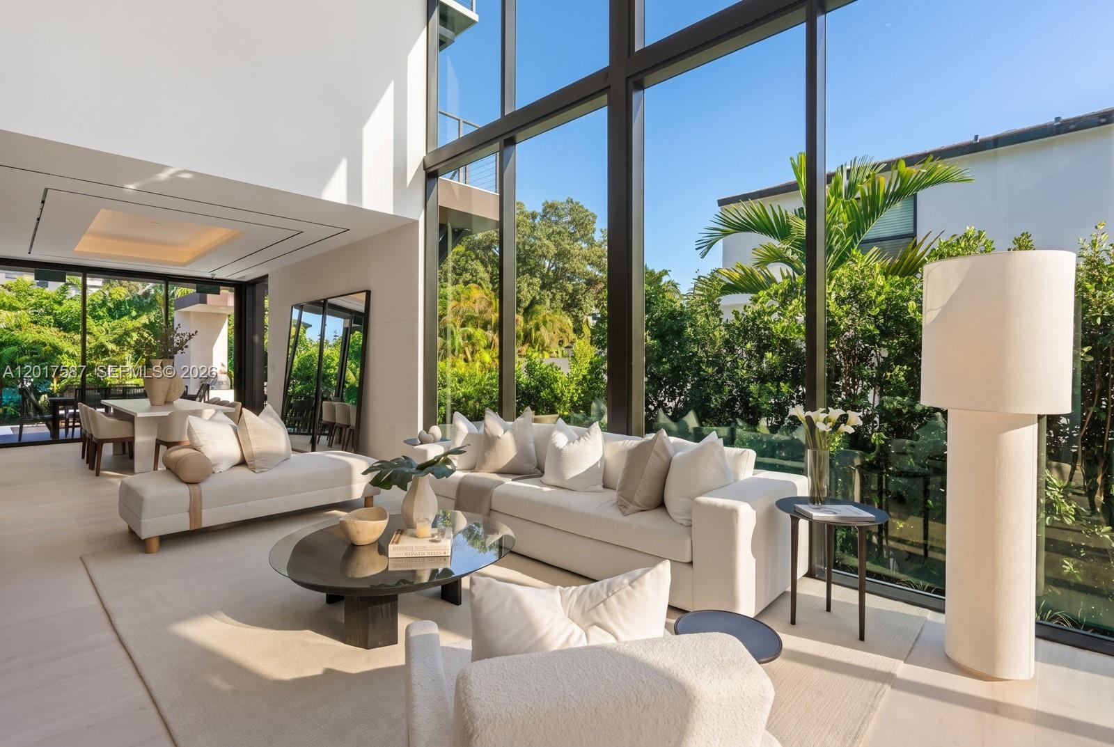A bright living room features floor-to-ceiling windows, white sofas, and a view of greenery — 3045 N Bay Rd, Miami Beach FL 33140, MIAMI BEACH, FL