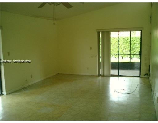 An empty living room with light-colored tile flooring and a sliding glass door to outside — 5702 Swordfish Cir, Tamarac FL 33319, TAMARAC, FL