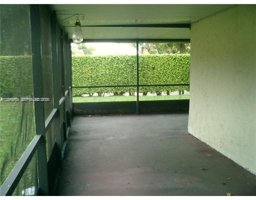 A screened-in porch features a concrete floor, a hanging light fixture, and a hedge view — 5702 Swordfish Cir, Tamarac FL 33319, TAMARAC, FL