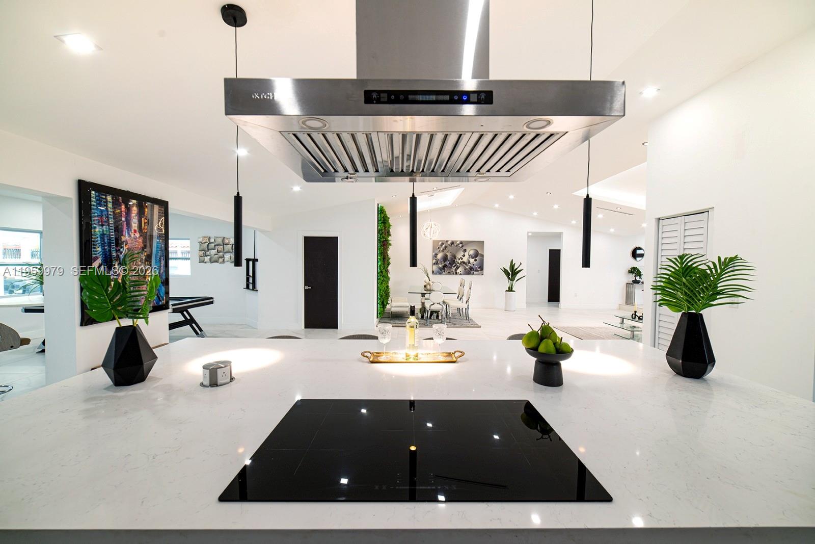 A modern kitchen island with a black cooktop overlooks an open-concept living and dining area — 3500 SW 111th Ave, Miami FL 33165, MIAMI, FL