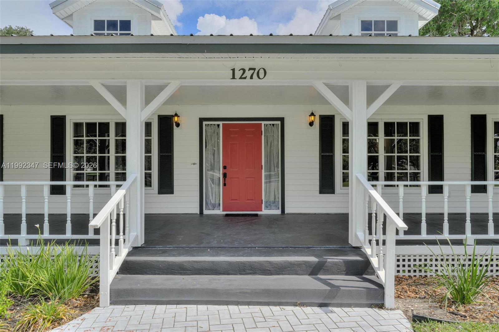 A white house exterior features a covered porch, a red front door, and black shutters — 1270 Riverbend Drive, La Belle FL 33935, LA BELLE, FL