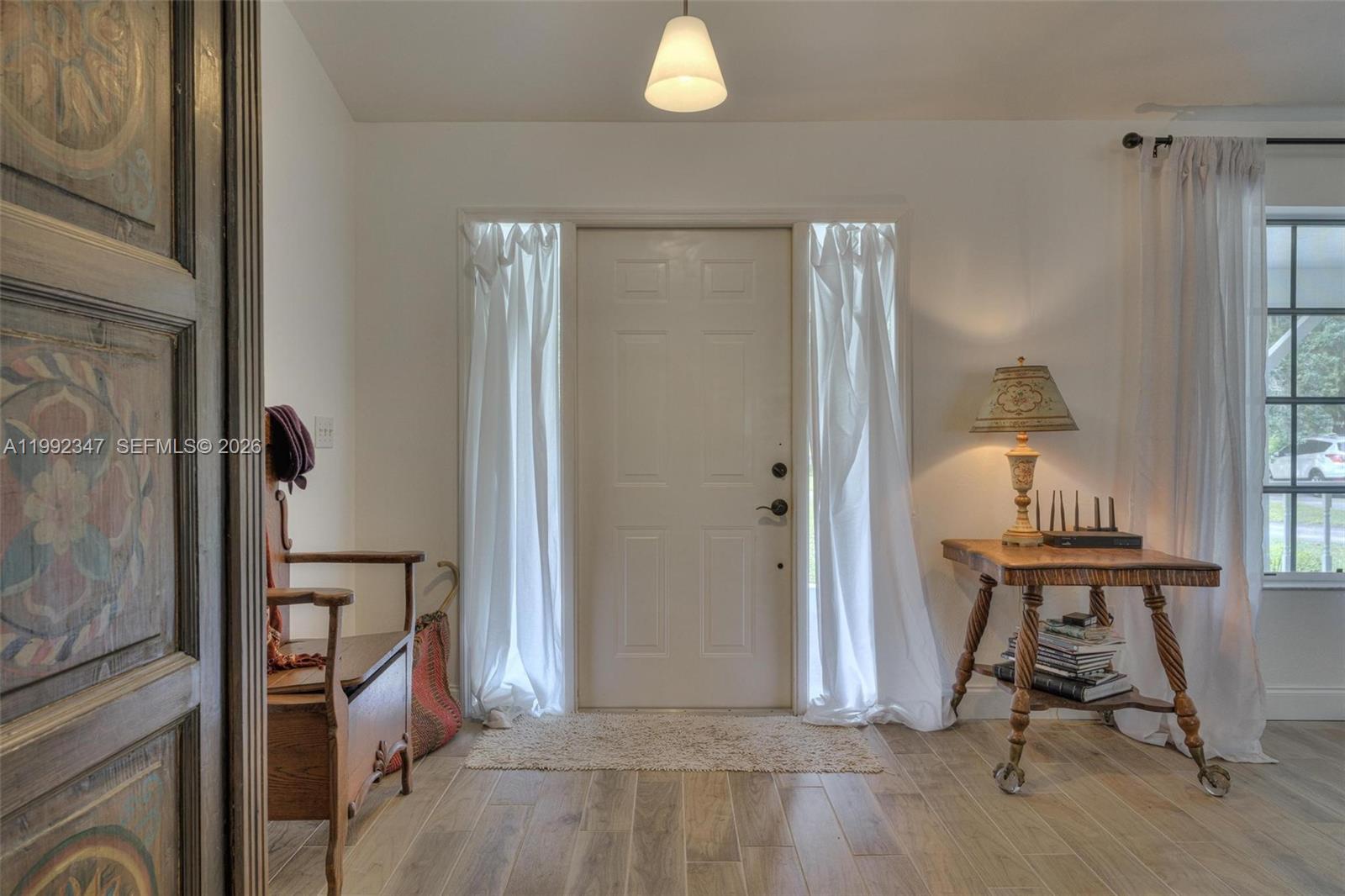 An entryway features a white front door with side curtains, a wooden bench, and a table — 1270 Riverbend Drive, La Belle FL 33935, LA BELLE, FL