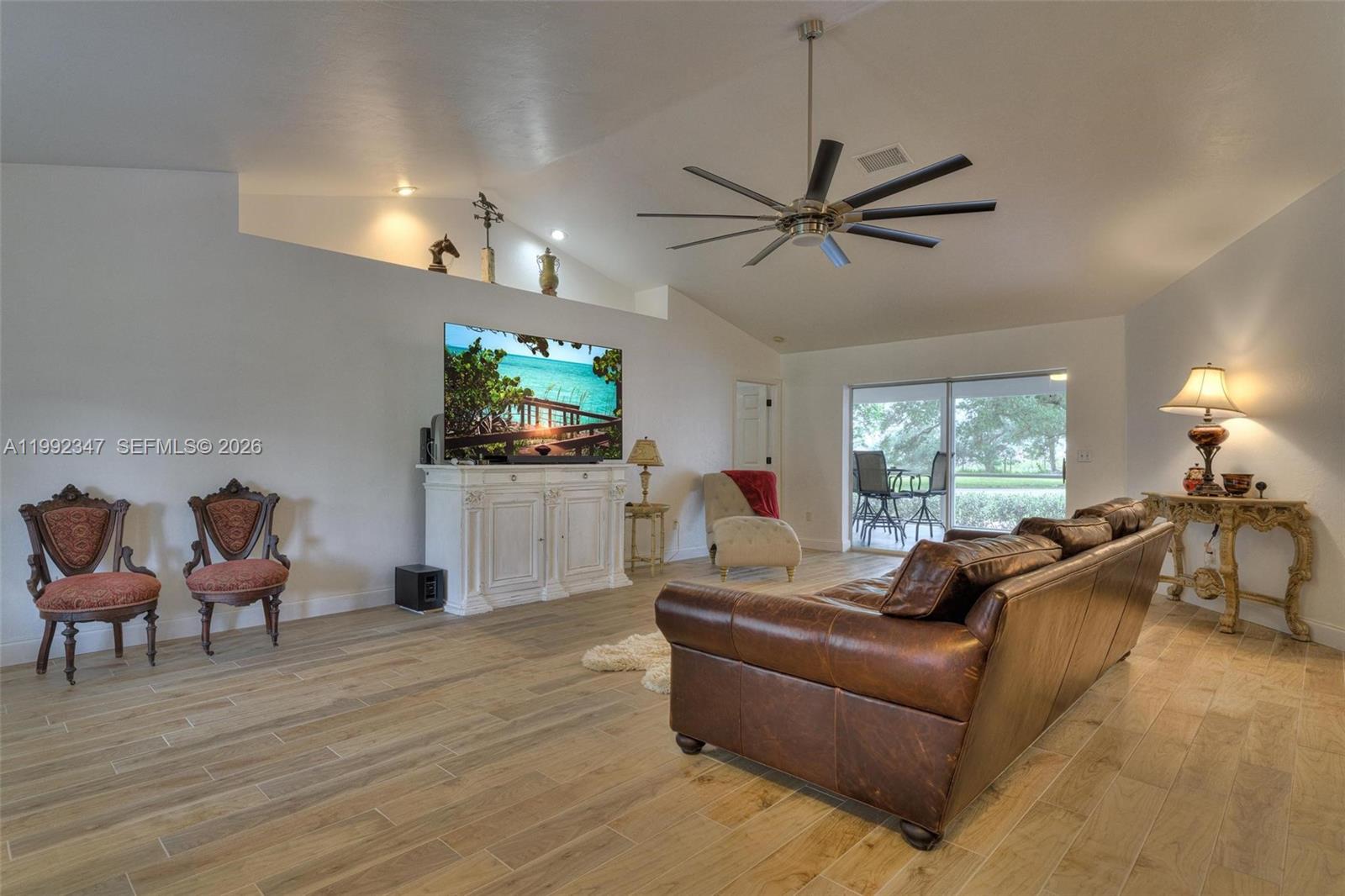 A living room features a leather sofa, wood-look tile flooring, and a vaulted ceiling — 1270 Riverbend Drive, La Belle FL 33935, LA BELLE, FL
