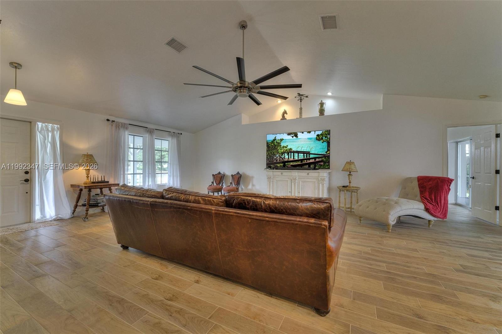A living room features a brown leather sofa, a ceiling fan, and a wall-mounted television — 1270 Riverbend Drive, La Belle FL 33935, LA BELLE, FL