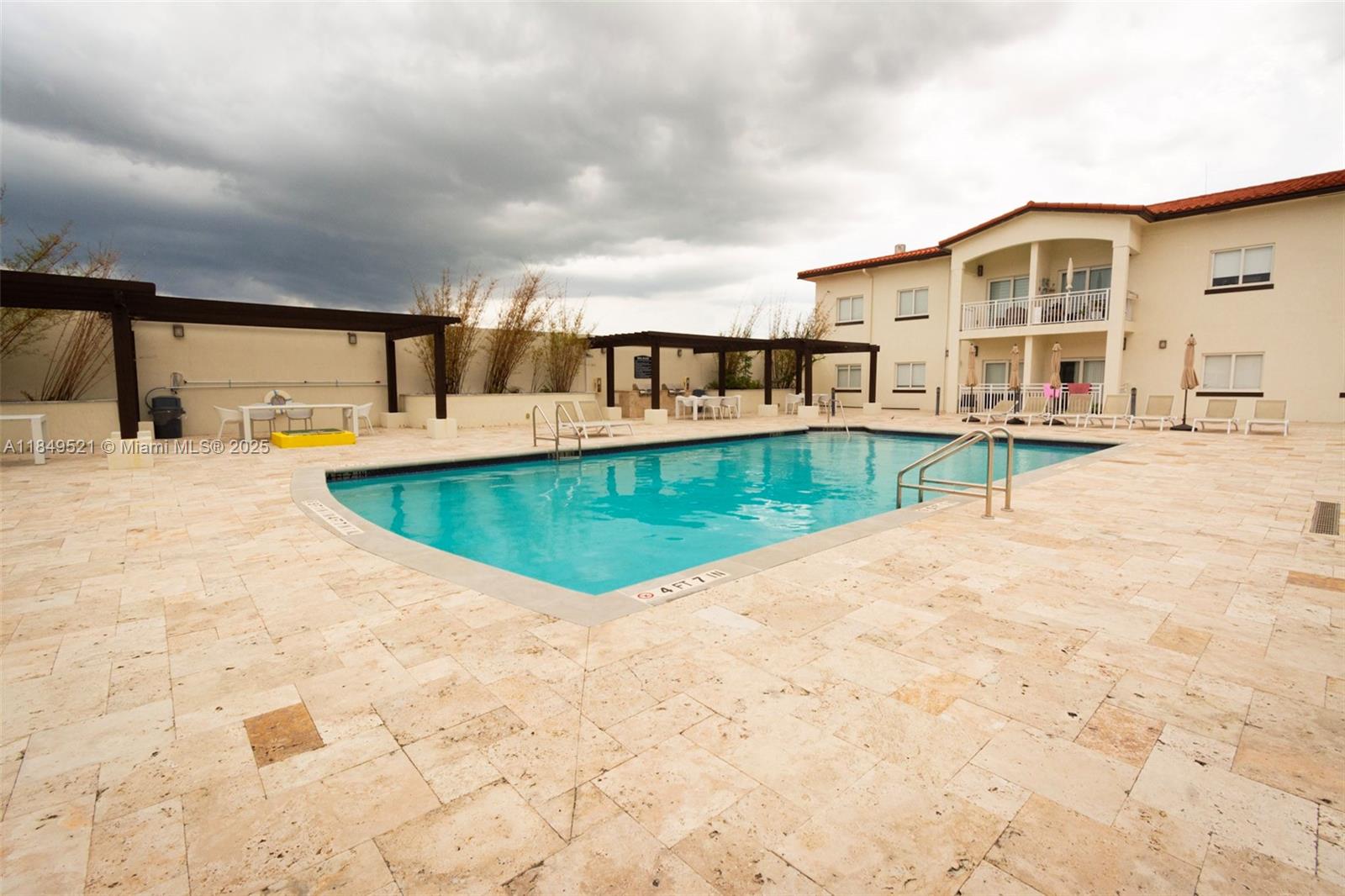 A rectangular swimming pool sits on a stone patio in front of a multi-story building — 10950 NW 82nd St # 405, Doral FL 33178, DORAL, FL