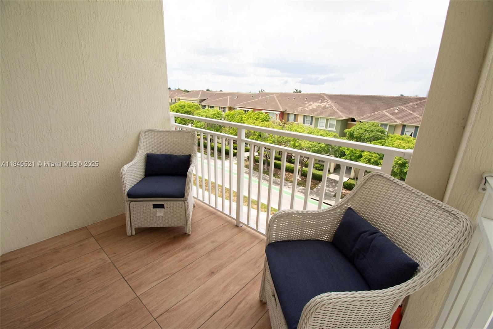 A balcony features two wicker chairs with navy cushions and wood-look tile flooring — 10950 NW 82nd St # 405, Doral FL 33178, DORAL, FL