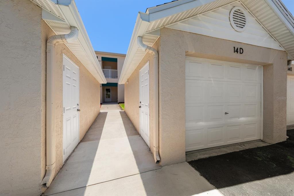 A concrete walkway leads between two beige garage buildings with white doors and gutters — 6330 99TH WAY N UNIT 14D, SEMINOLE, FL