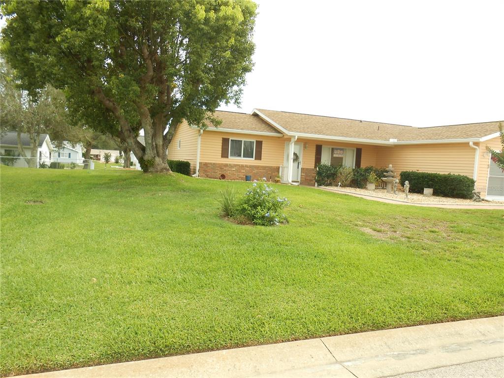 A single-story house with light yellow siding, a brick base, and a large front yard — 9826 SE 178TH LANE, SUMMERFIELD, FL
