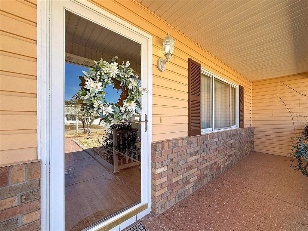 A front porch features a white storm door with a wreath, siding, and brick accents — 9826 SE 178TH LANE, SUMMERFIELD, FL