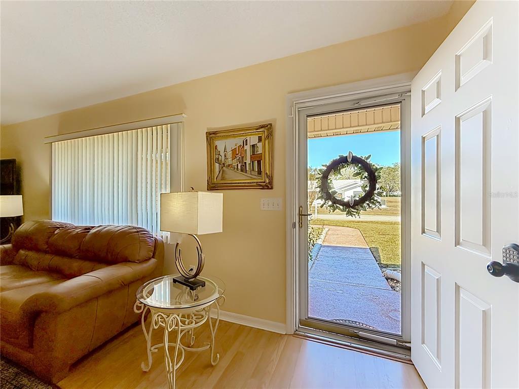 A living room with a brown sofa, glass side table, and an open front door — 9826 SE 178TH LANE, SUMMERFIELD, FL