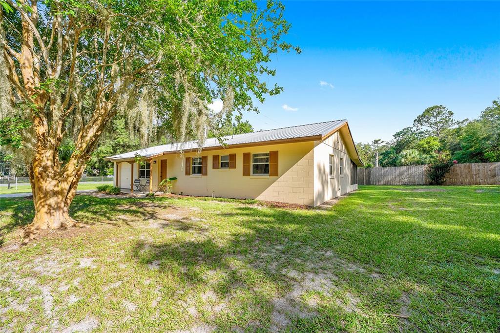 A single-story house with a metal roof and tan exterior sits on a grassy lot — 2420 NE 38TH STREET, OCALA, FL