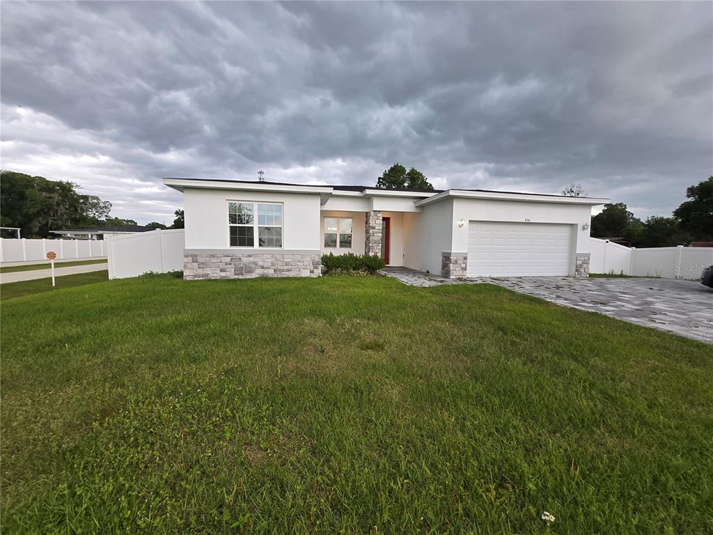 A single-story house with white stucco walls, stone accents, and a two-car garage — 890 E 19TH STREET, ST CLOUD, FL