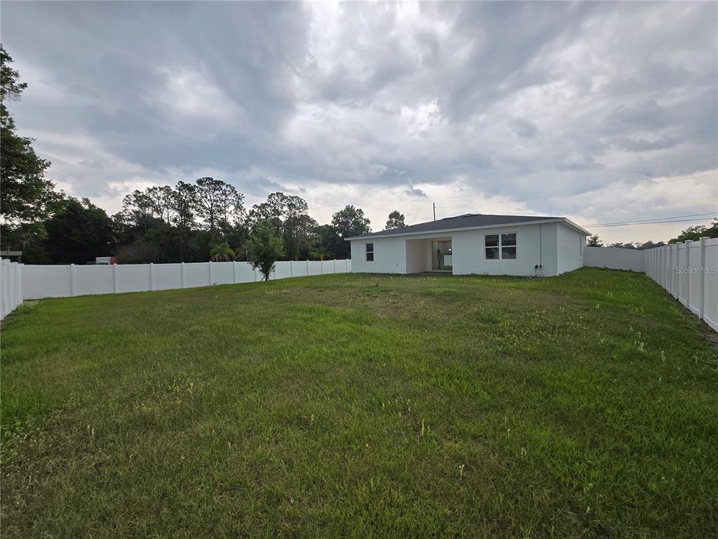 A white house sits in a large, grassy backyard enclosed by a white vinyl fence — 890 E 19TH STREET, ST CLOUD, FL