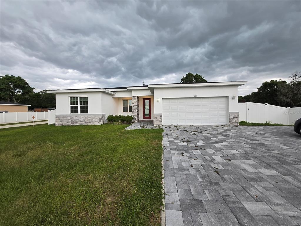 A single-story house with white stucco, stone accents, a red front door, and paver driveway — 890 E 19TH STREET, ST CLOUD, FL