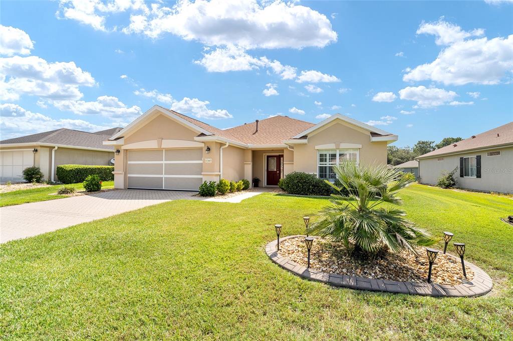 A single-story suburban house with a tan stucco exterior, a two-car garage, and a palm tree — 12603 SE 90TH TERRACE, SUMMERFIELD, FL