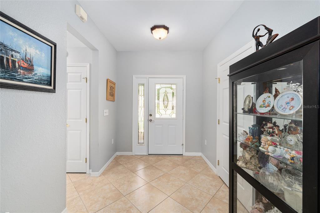 A bright entryway features light-colored tile flooring, a white front door, and a glass display cabinet — 12603 SE 90TH TERRACE, SUMMERFIELD, FL