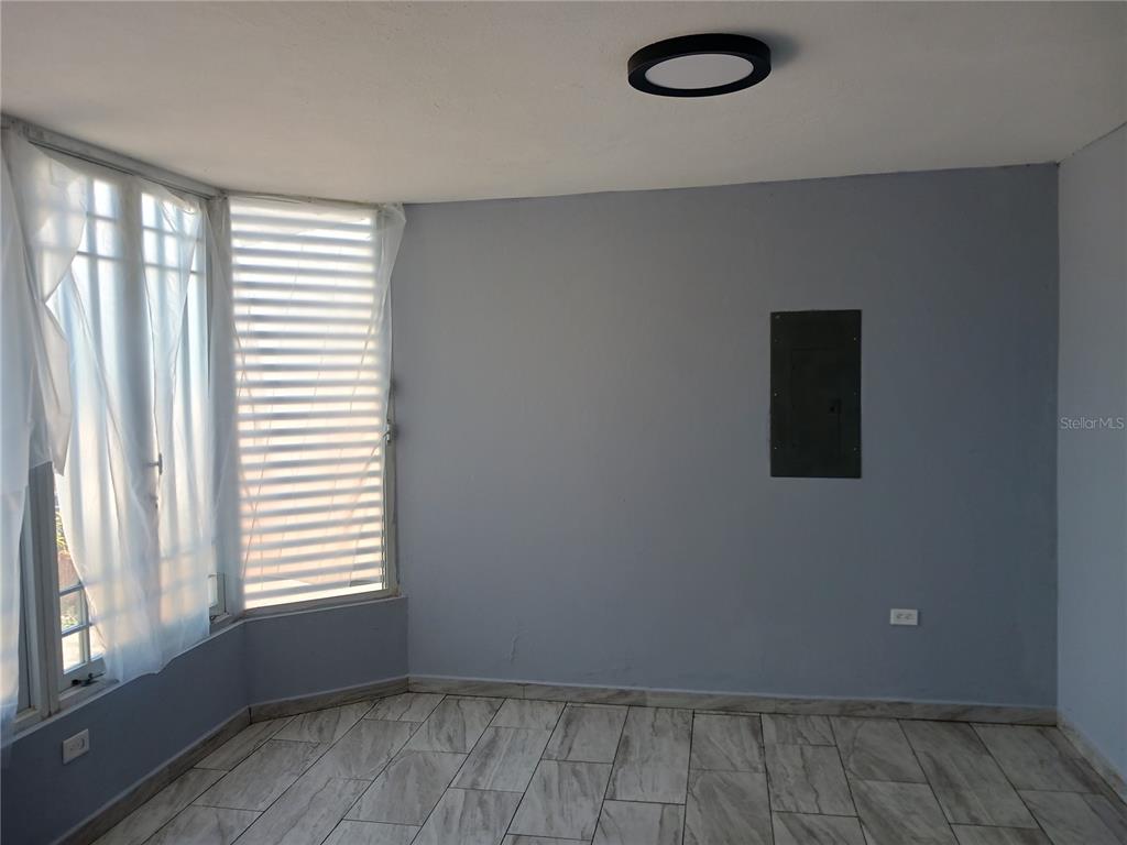 An empty room features light gray walls, wood-look tile flooring, and a large window — KM. 11.7 RD. 174 INT, BAYAMON, PR