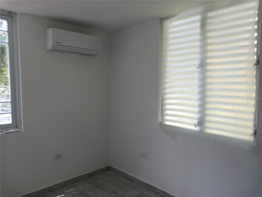 A room with white walls, tile flooring, a wall-mounted air conditioner, and two windows — KM. 11.7 RD. 174 INT, BAYAMON, PR