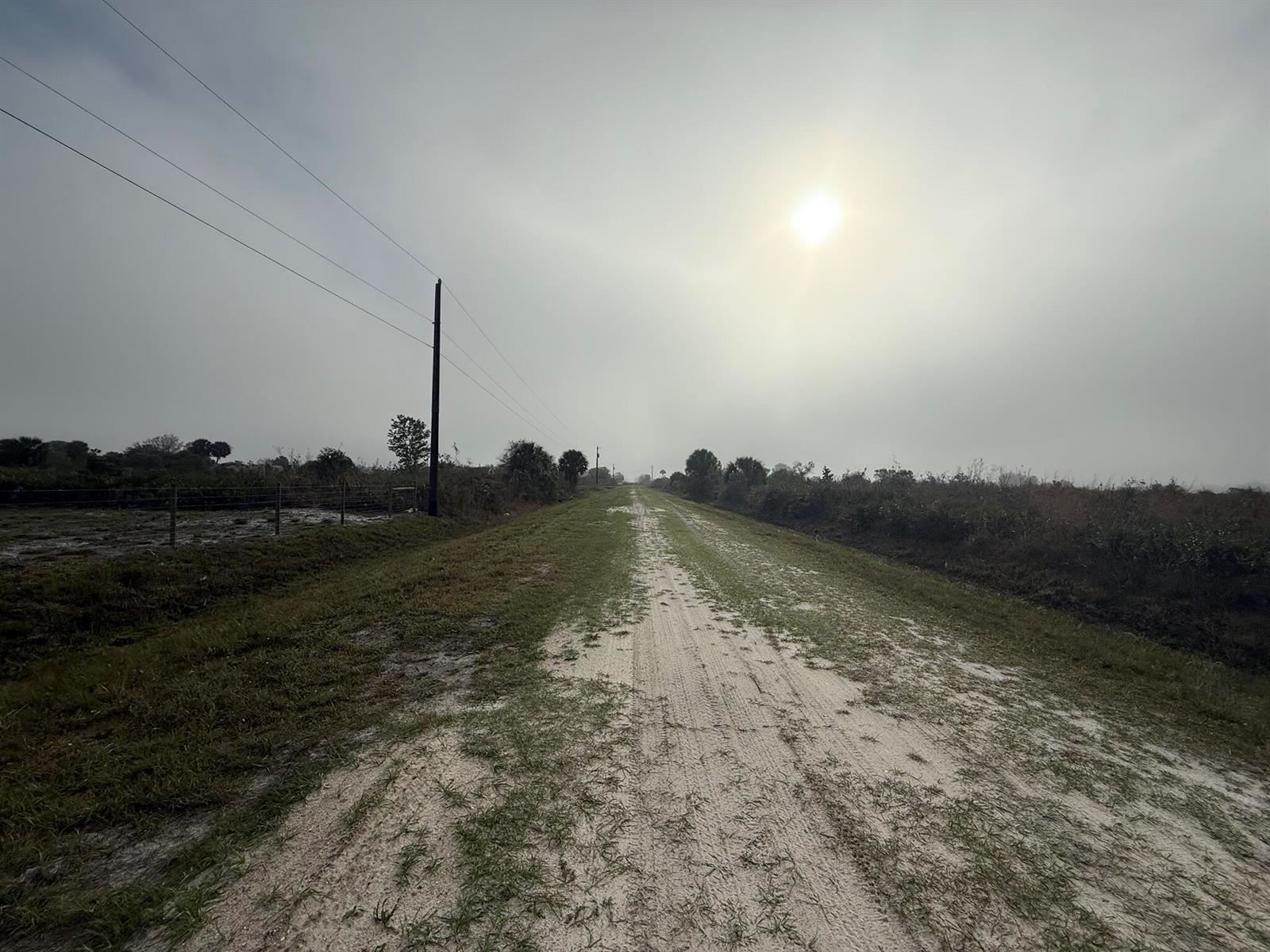 A dirt path stretches through a grassy, open field under a hazy, sunlit sky — 18935 NW 268th Street, Okeechobee FL 34972, OKEECHOBEE, FL