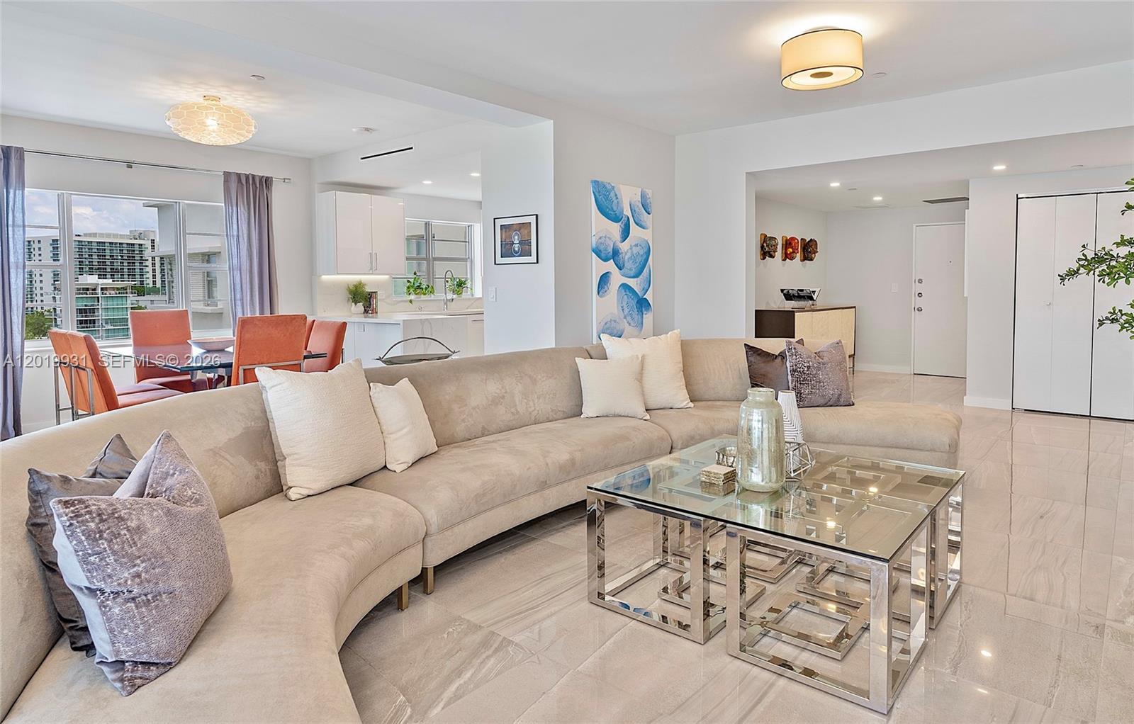 A modern living room features a large curved beige sectional sofa and glass coffee tables — 16 Island Ave # 7C, Miami Beach FL 33139, MIAMI BEACH, FL
