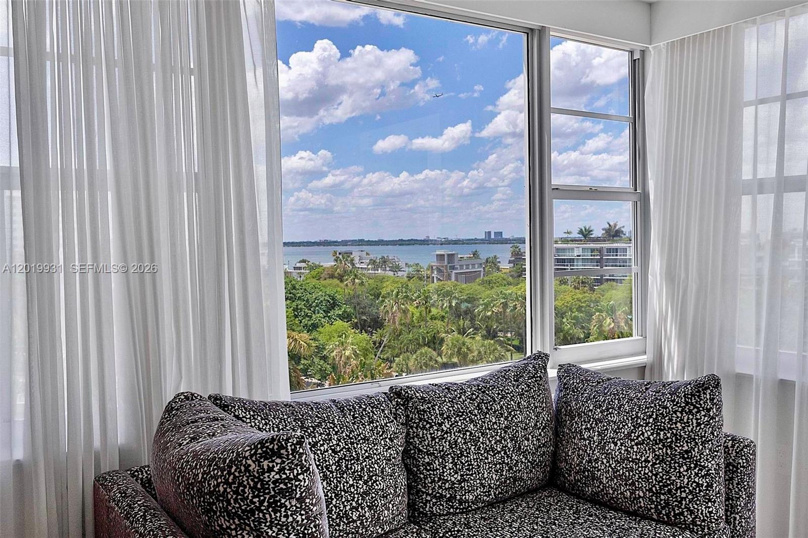 A patterned sofa sits in front of a large window overlooking trees and water — 16 Island Ave # 7C, Miami Beach FL 33139, MIAMI BEACH, FL