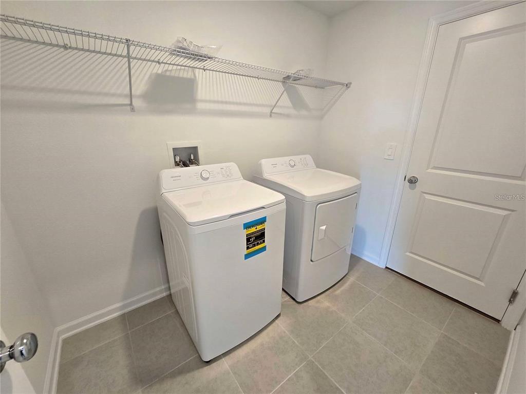 A laundry room features a white washer and dryer, tile flooring, and wire shelving — 3676 ROLLING RIDGE BEND, DAVENPORT, FL