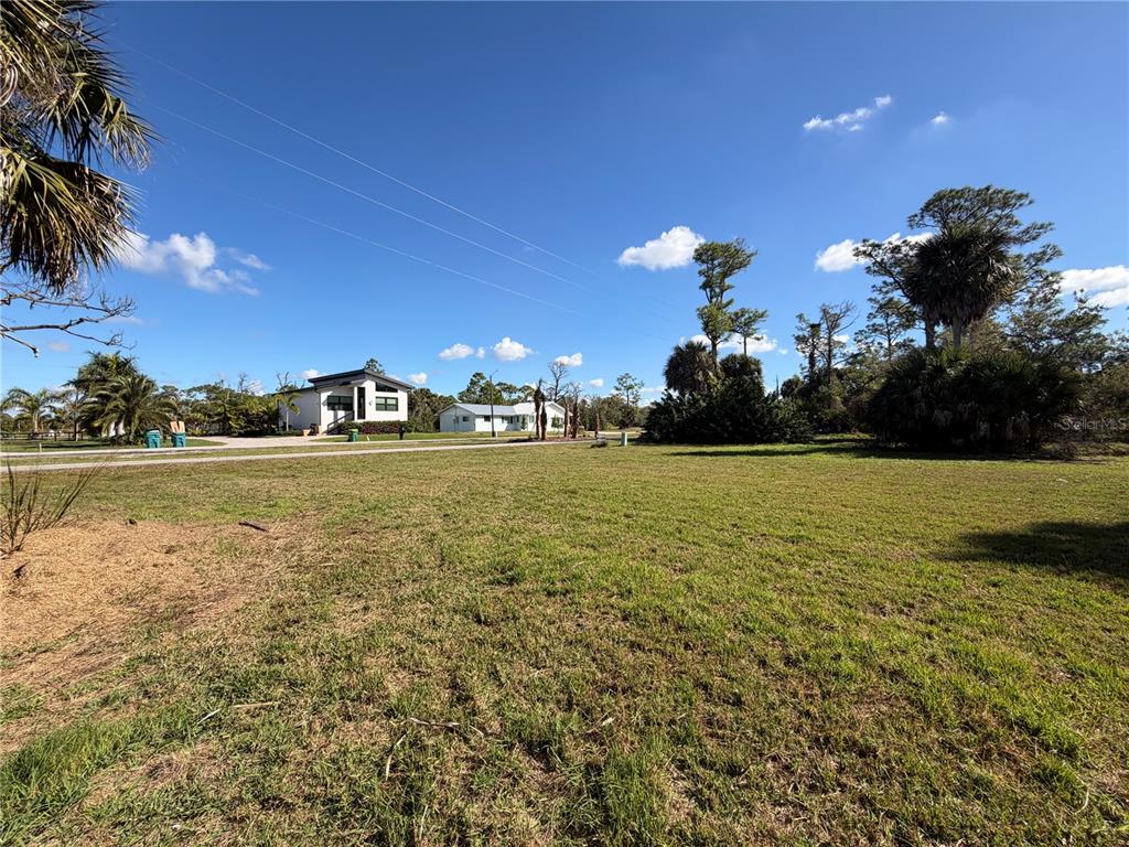 A grassy vacant lot sits in front of a road with two houses in the distance — 24501 YACHT CLUB BOULEVARD, PUNTA GORDA, FL