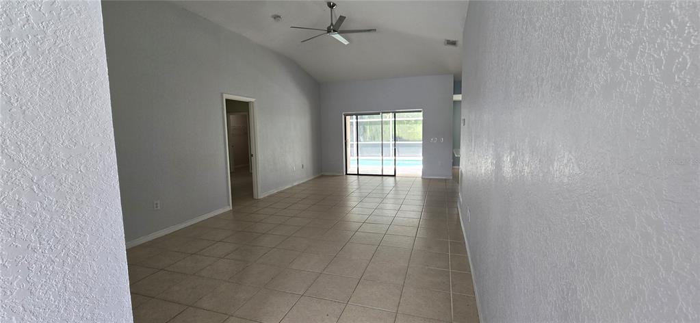 An empty living room with light-colored tile flooring, vaulted ceilings, and sliding glass patio doors — 334 RESERVE DRIVE, DAVENPORT, FL