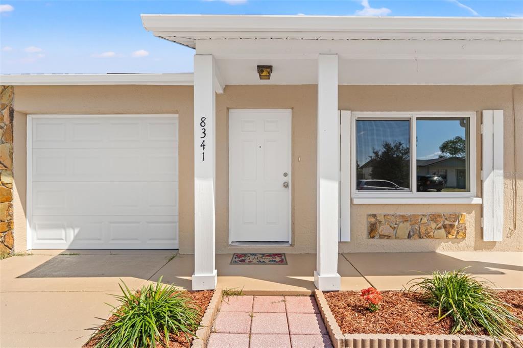 The exterior of a house features a white front door, a garage, and stone accents — 8341 CORNEY DRIVE, PORT RICHEY, FL