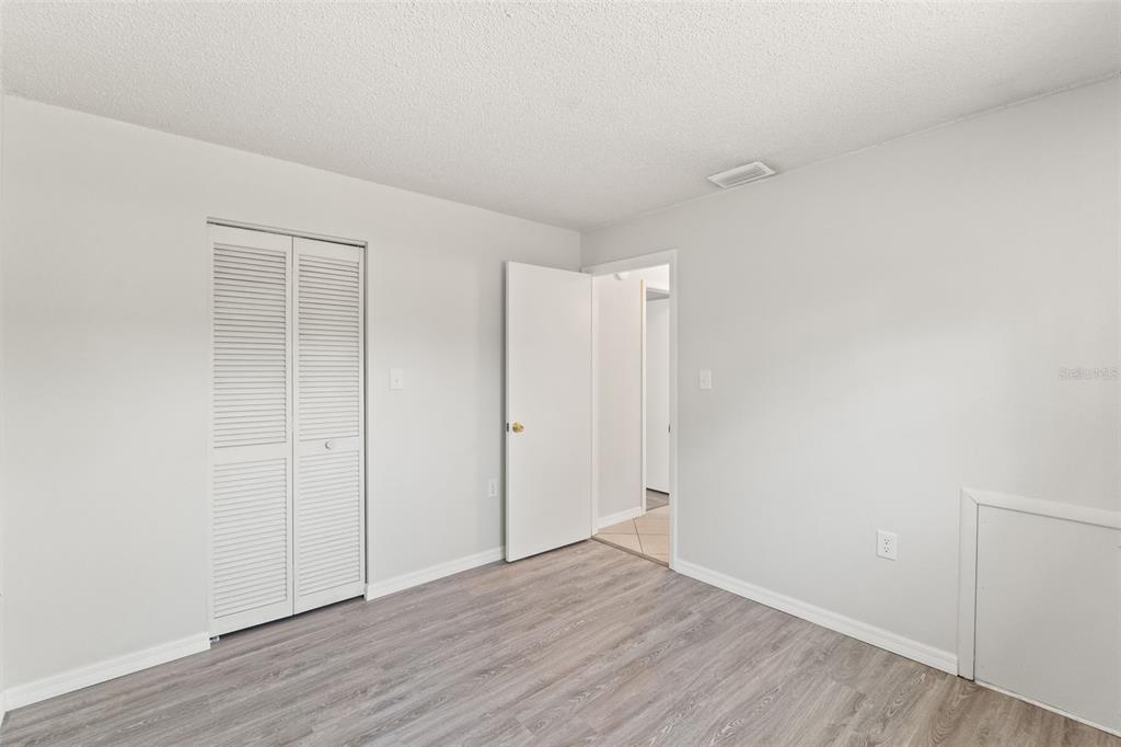 A bedroom with light gray walls, wood-look flooring, a white closet, and an open doorway — 8341 CORNEY DRIVE, PORT RICHEY, FL