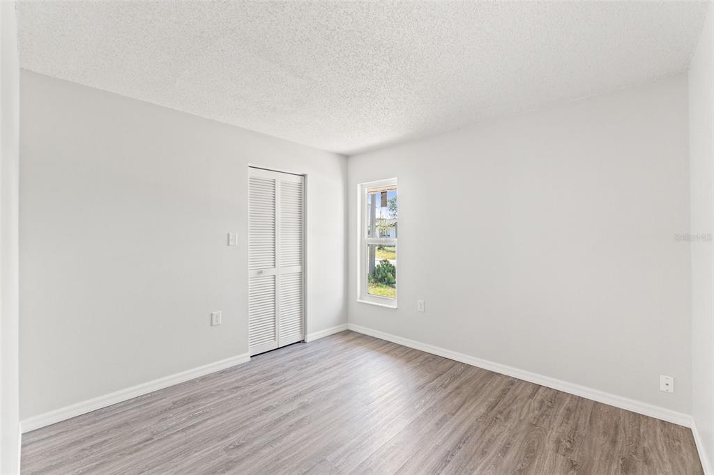 A bedroom with light gray walls, wood-look flooring, a white louvered closet door, and a window — 8341 CORNEY DRIVE, PORT RICHEY, FL