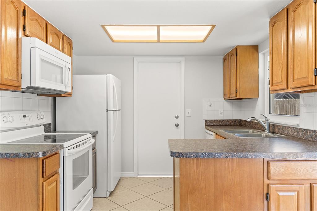 A kitchen features wood cabinets, white appliances, a laminate countertop, and a tile floor — 8341 CORNEY DRIVE, PORT RICHEY, FL