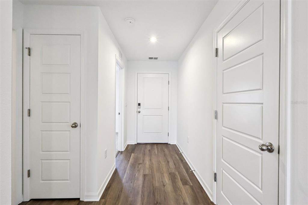 A hallway with white walls, wood-look flooring, and three white interior doors — 1134 AMBER WAVES COURT, LAKE WALES, FL
